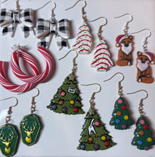 Load image into Gallery viewer, A collection of handmade Christmas-themed dangle earrings displayed on a white background. The designs include green Christmas trees with colorful ornaments, red and white striped candy canes, black and white bow earrings, and fox and deer pendants.
